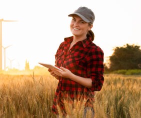 A woman farmer examines the field of cereals and sends data to the cloud from the tablet. Smart farming and digital agriculture.